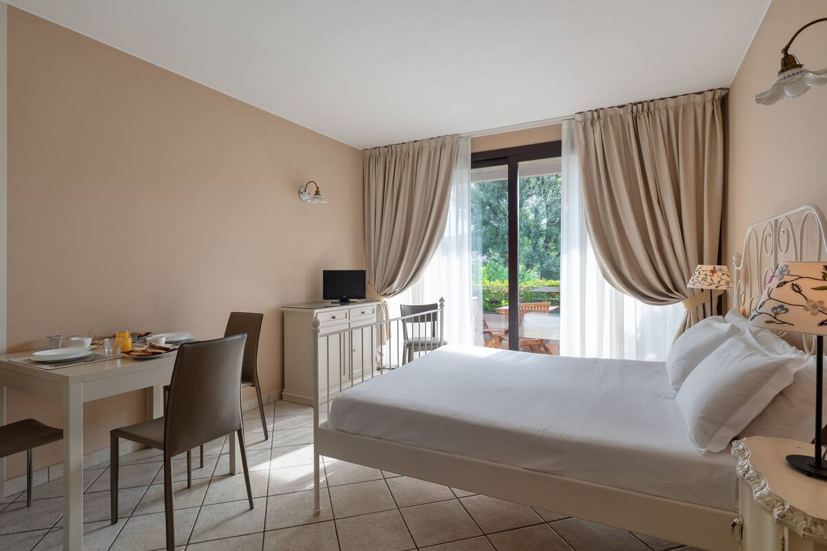 Ein Hotelzimmer mit Bett, Schreibtisch, Sessel, Fernseher und Blick ins Freie.
