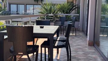 Ein Außenbereich mit Terrasse, einem Tisch, Stühlen, einem Fliesenboden und Blick auf ein Gebäude mit einem Ziegeldach.