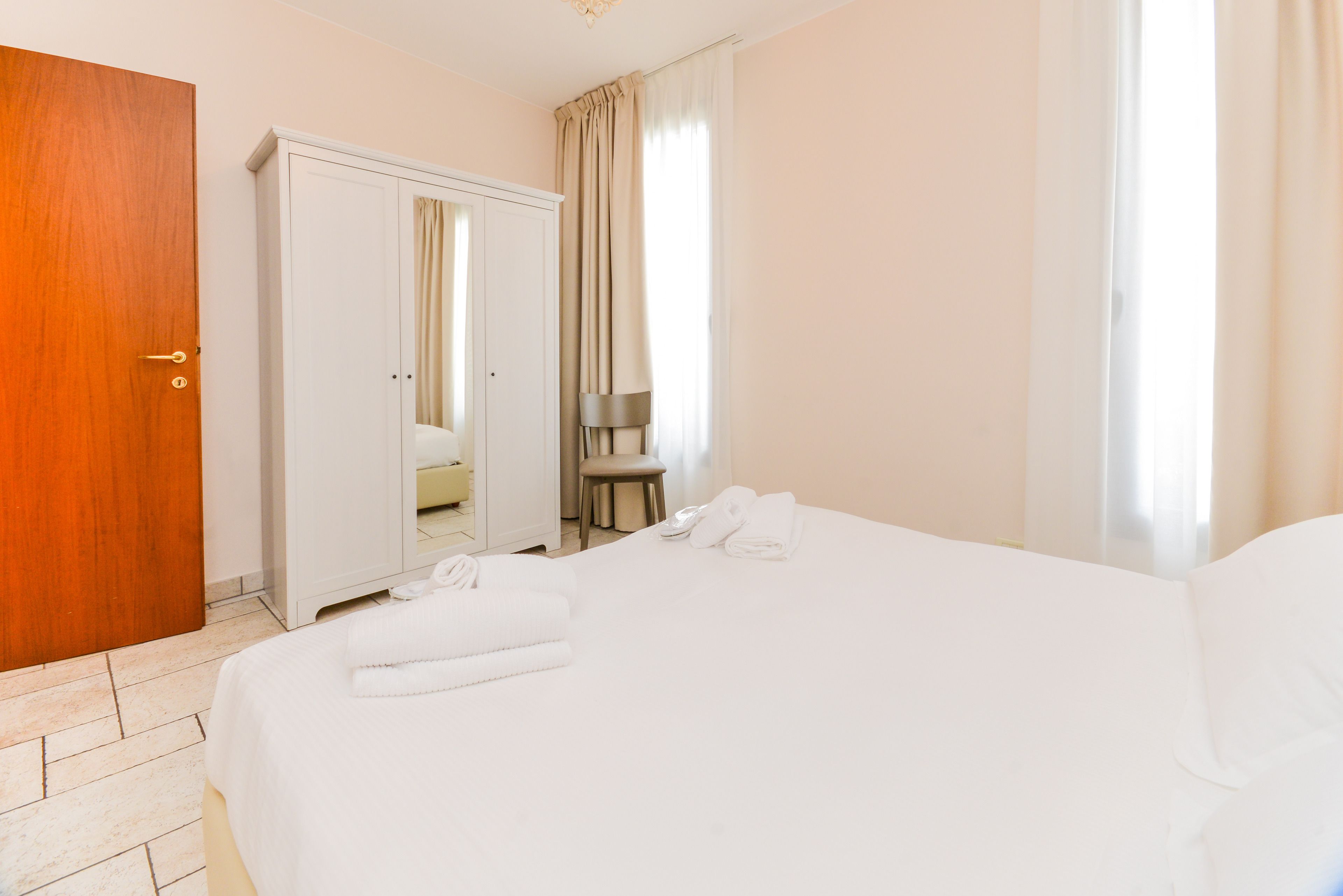Une chambre d’hôtel avec un grand lit, une porte en bois, une armoire et une salle de bain visible à travers une porte ouverte.