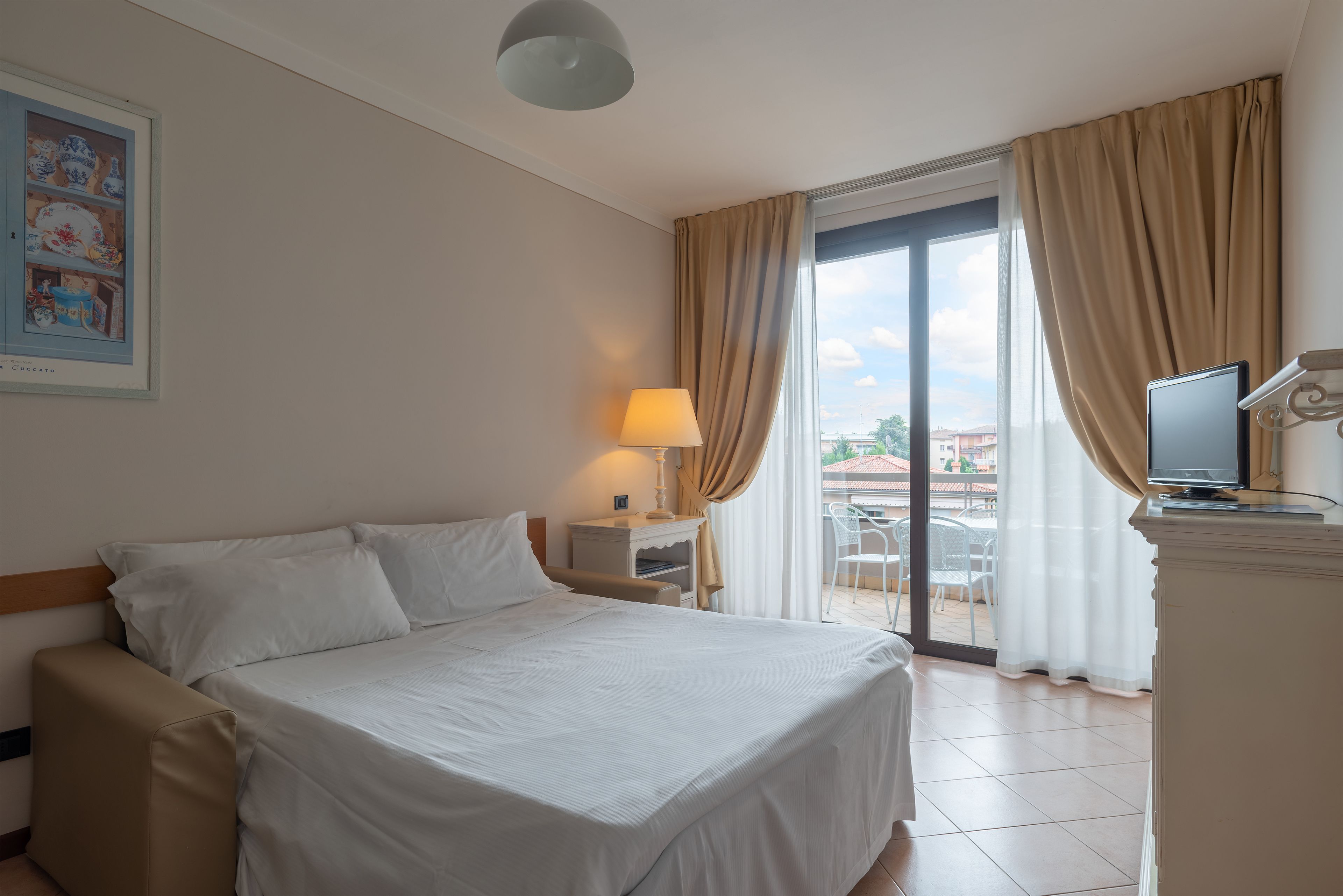 A hotel room with a bed, a desk with a lamp, a television, and a view of the outdoors.
