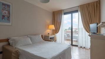 A hotel room with a bed, a desk with a lamp, a television, and a view of the outdoors.