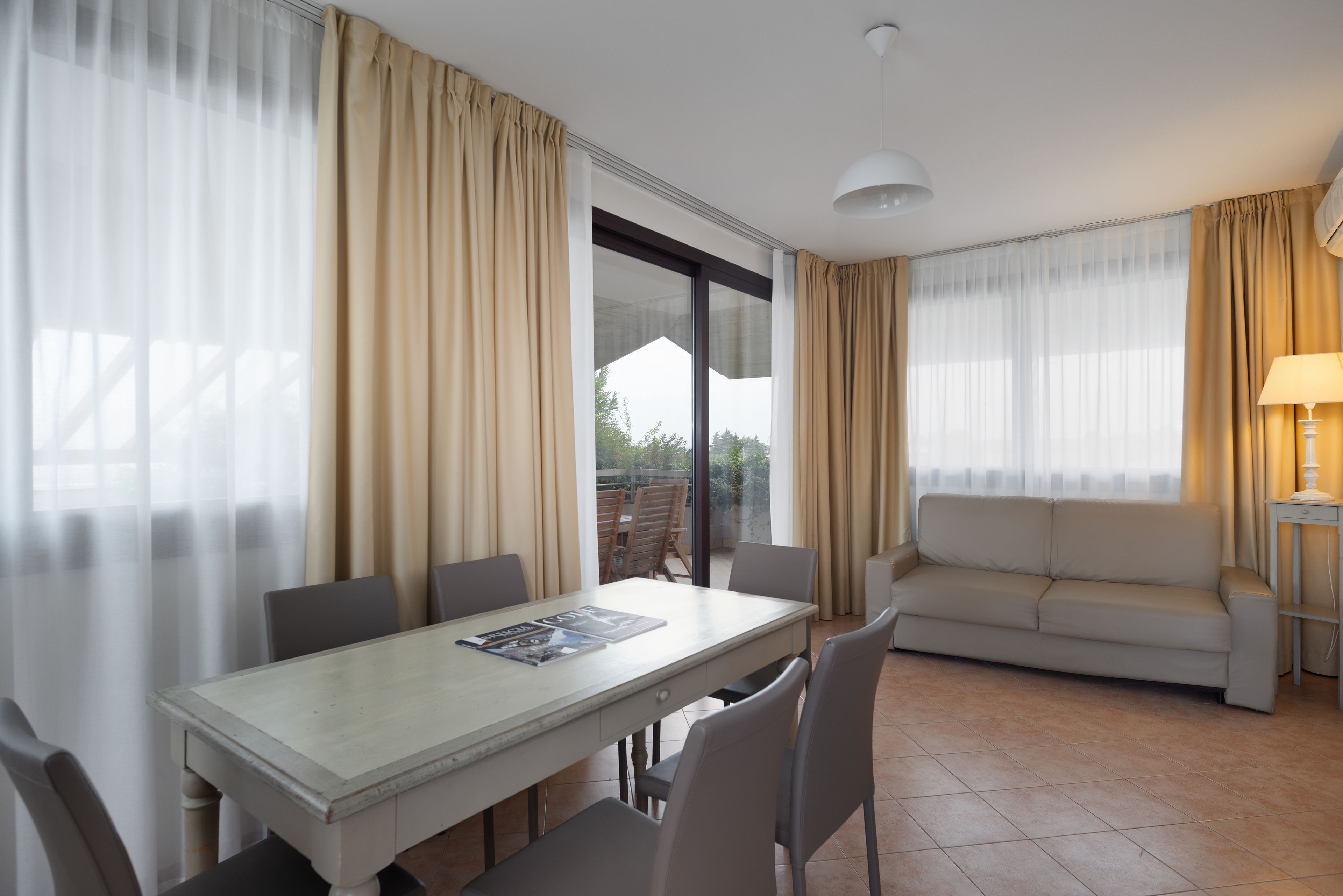 A room with a dining table, chairs, a sofa, and a lamp.
