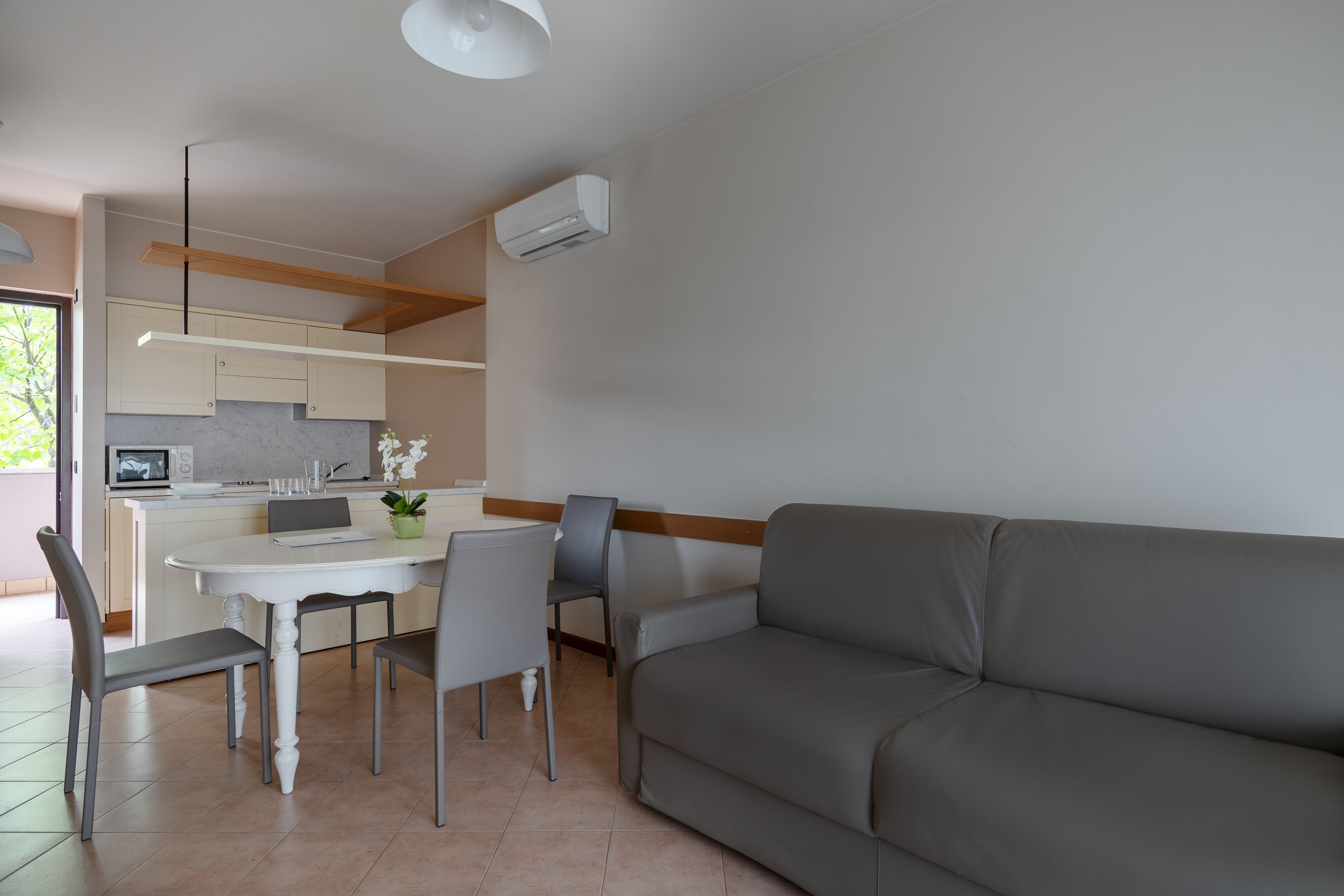 Et moderne køkken med spiseplads, en grå sofa og en hvid ventilator.