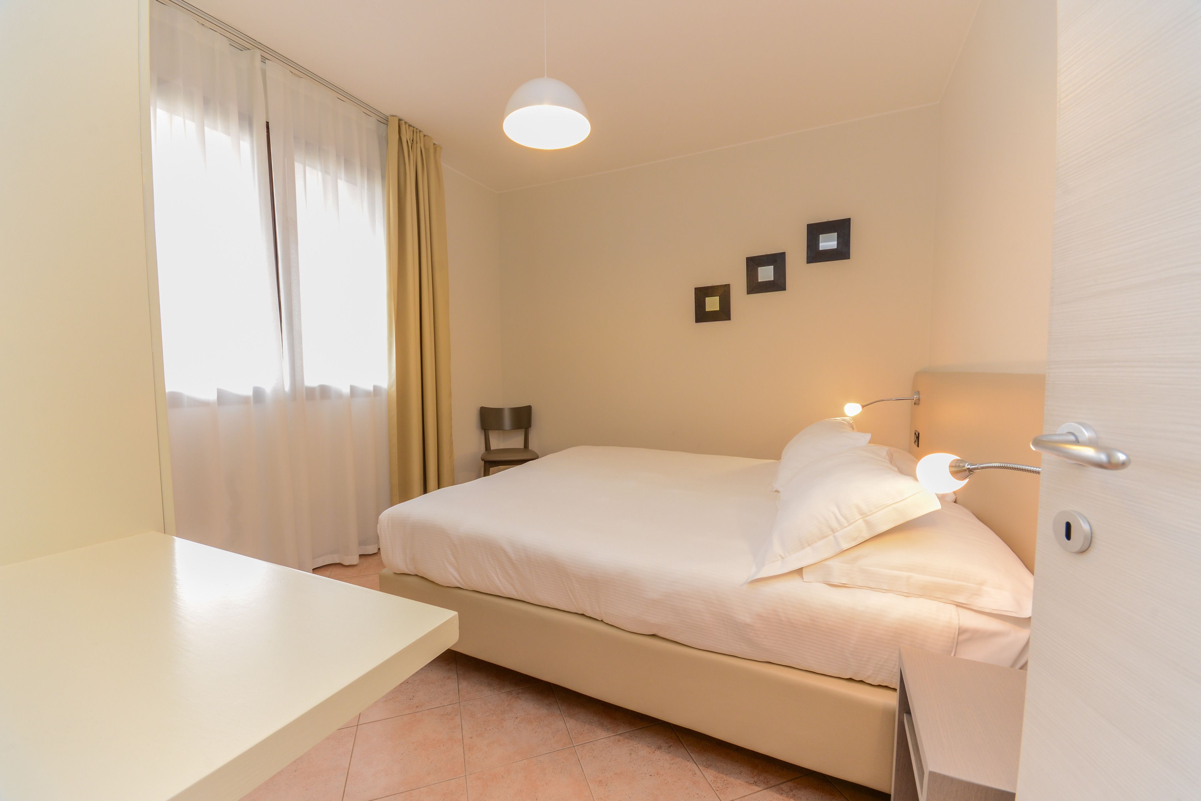 Une chambre à coucher avec un lit, une table de chevet, des rideaux et une lampe fixée au mur.