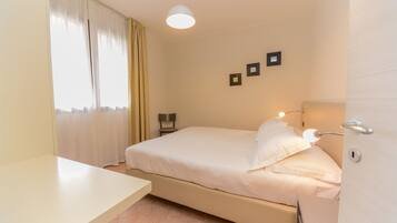 Une chambre à coucher avec un lit, une table de chevet, des rideaux et une lampe fixée au mur.