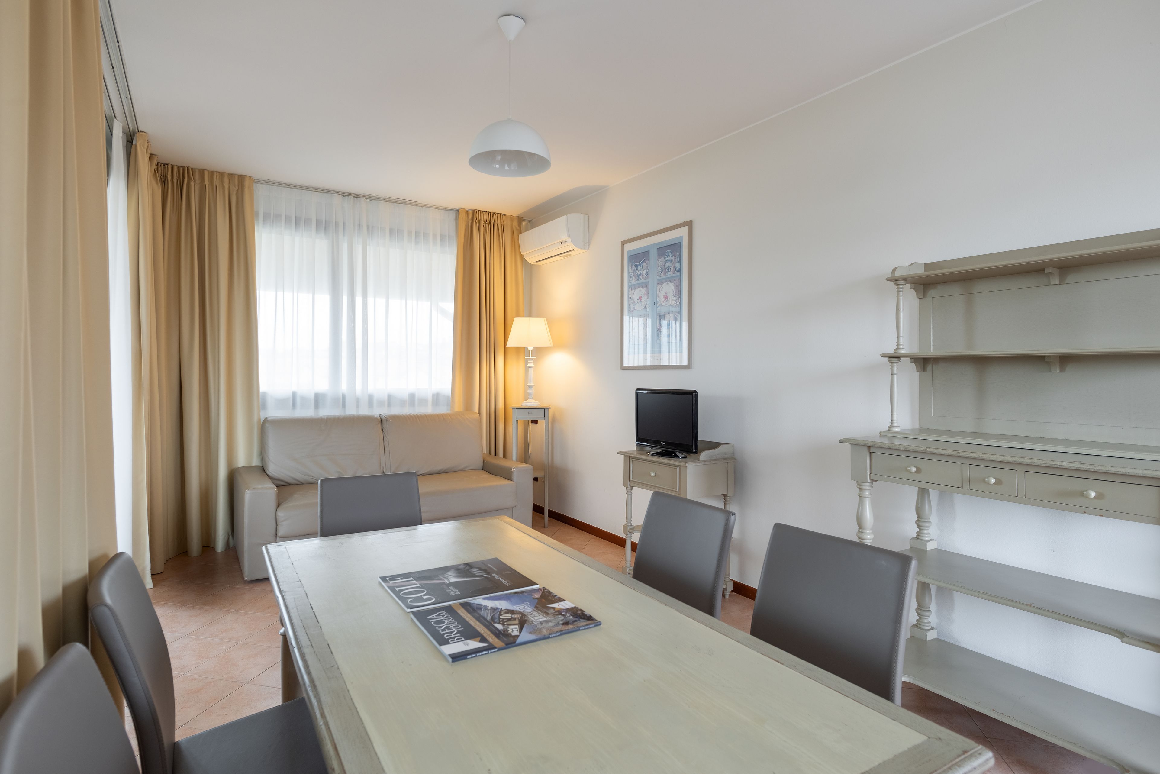 A hotel room with a dining table, chairs, a sofa, a TV, and a lamp.