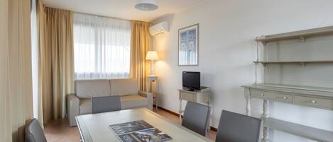 A hotel room with a dining table, chairs, a sofa, a TV, and a lamp.