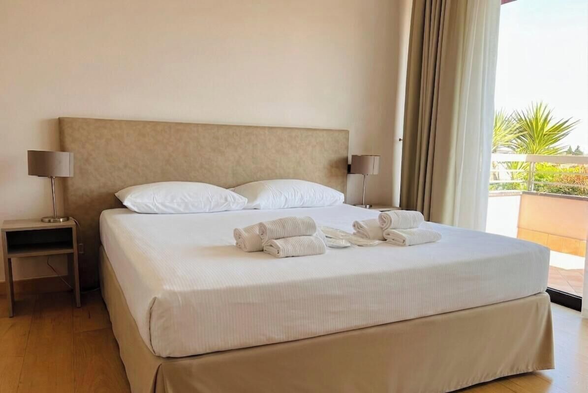 Ein Hotelzimmer mit einem großen Bett, zwei Nachttischen und Blick ins Freie.