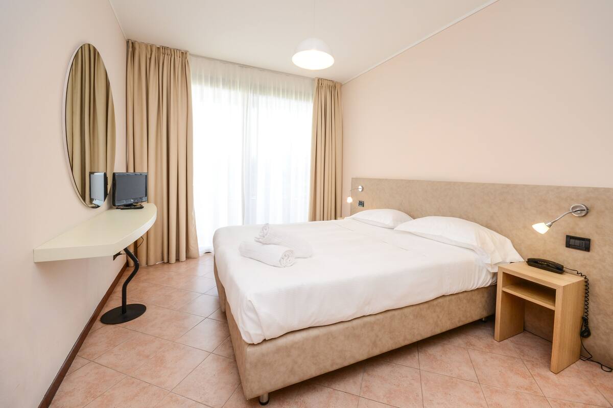 Ein Hotelzimmer mit Bett, Nachttisch, Lampe und Fernseher auf einem Schreibtisch.