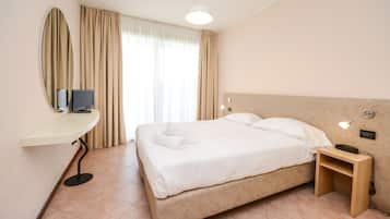Una habitación de hotel con cama, mesita de noche, lámpara y televisor sobre un escritorio.