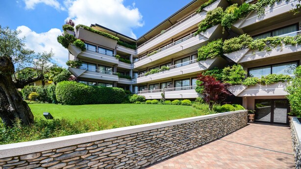 A multi-story hotel with balconies adorned with greenery, a stone retaining wall, and a well-maintained lawn. - Il Sogno Apartments (Desenzano del Garda)