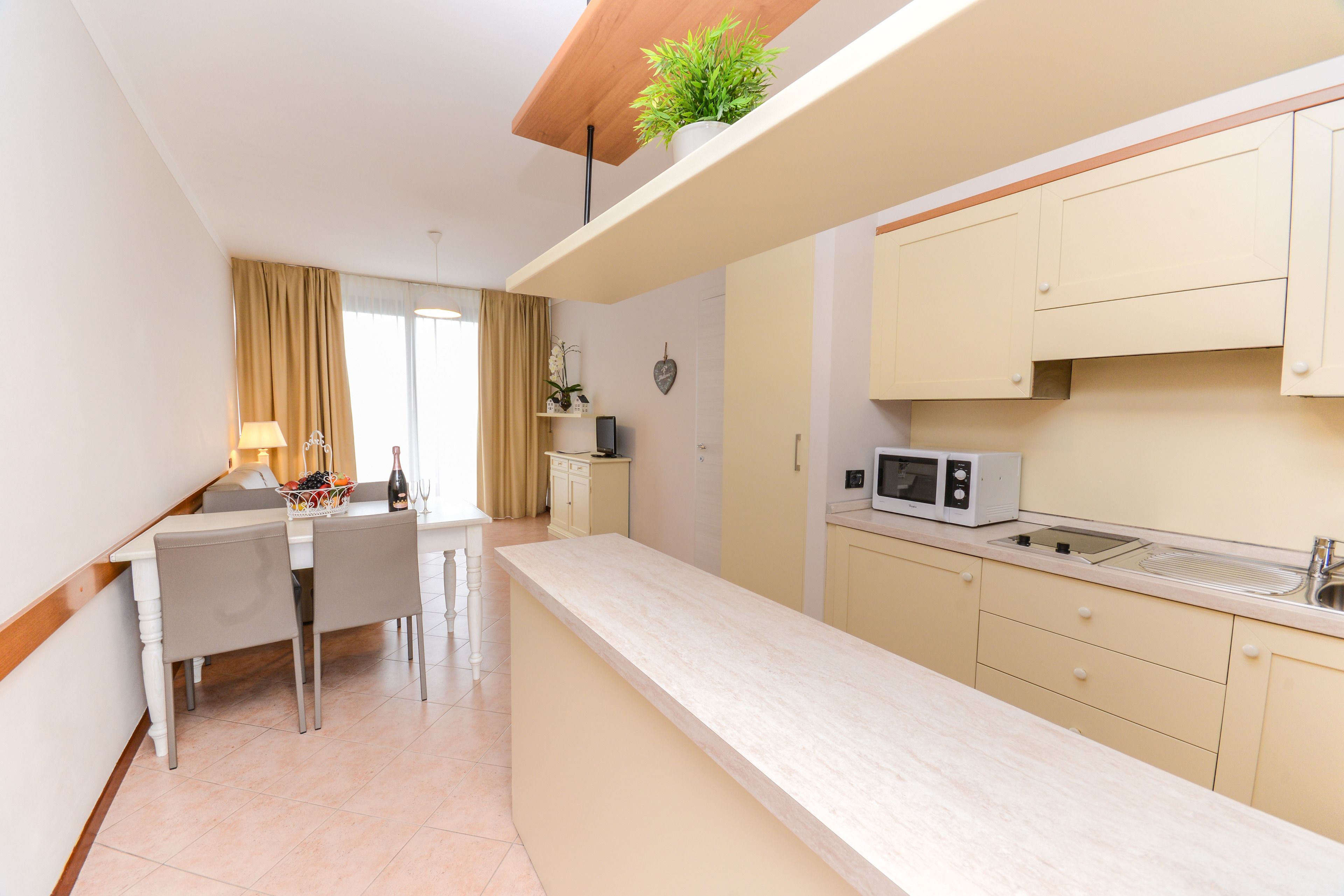 Une cuisine compacte avec un coin repas, comprenant un four à micro-ondes, un évier et une plante en pot placée sur une étagère.