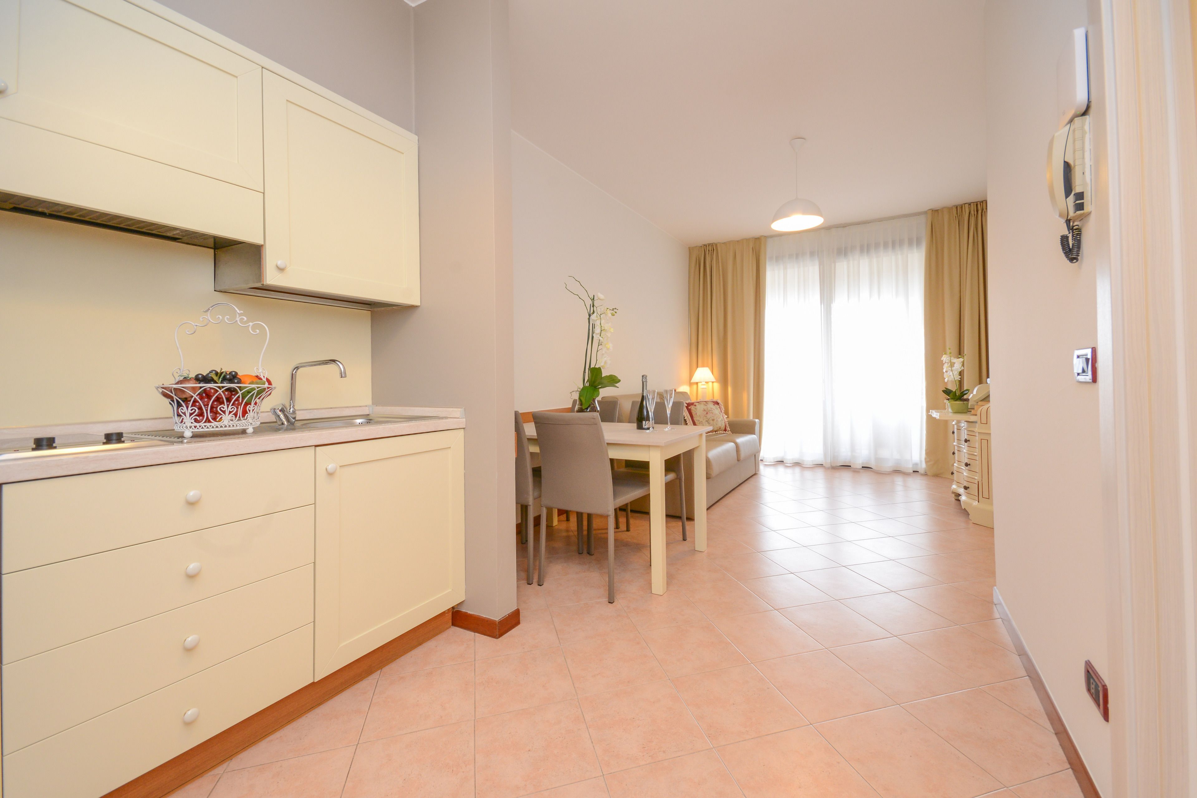 Una cucina moderna con mobili bianchi, un'area pranzo con tavolo e sedie, e un soggiorno con divano e tende.