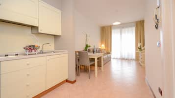 Una cucina moderna con mobili bianchi, un'area pranzo con tavolo e sedie, e un soggiorno con divano e tende.