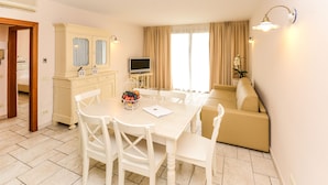 A dining area with a table and chairs, a television on a stand, and a sofa in the background. - Il Sogno Apartments (Desenzano del Garda)