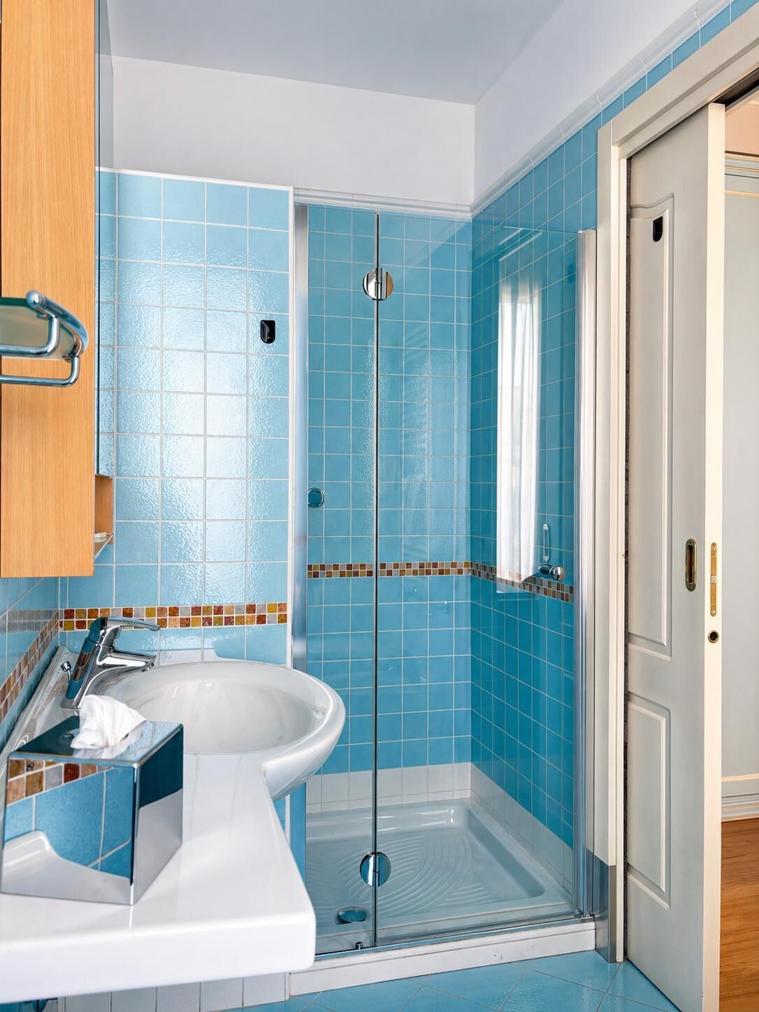 Ein Badezimmer mit Duschkabine aus Glas, einem weißen Waschbecken und blauen Fliesen an den Wänden.