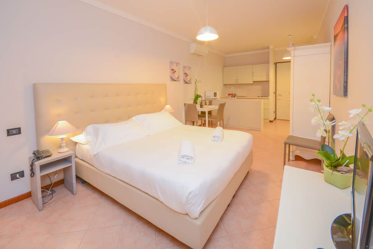 Ein Hotelzimmer mit Bett, Nachttisch, Lampe und einem kleinen Schreibtisch mit Pflanze.