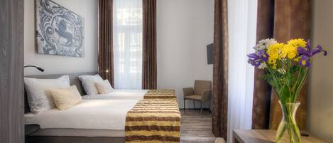 A hotel room with a bed, a bedside table with a vase of flowers, a chair, and a painting on the wall.