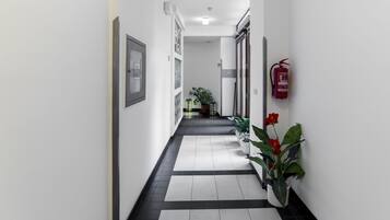 A hallway with a tiled floor, framed pictures on the walls, a potted plant, and a fire extinguisher.