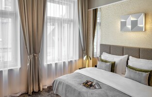 Een hotelkamer met een groot bed, een hoofdbord, een wandlamp en dunne gordijnen.