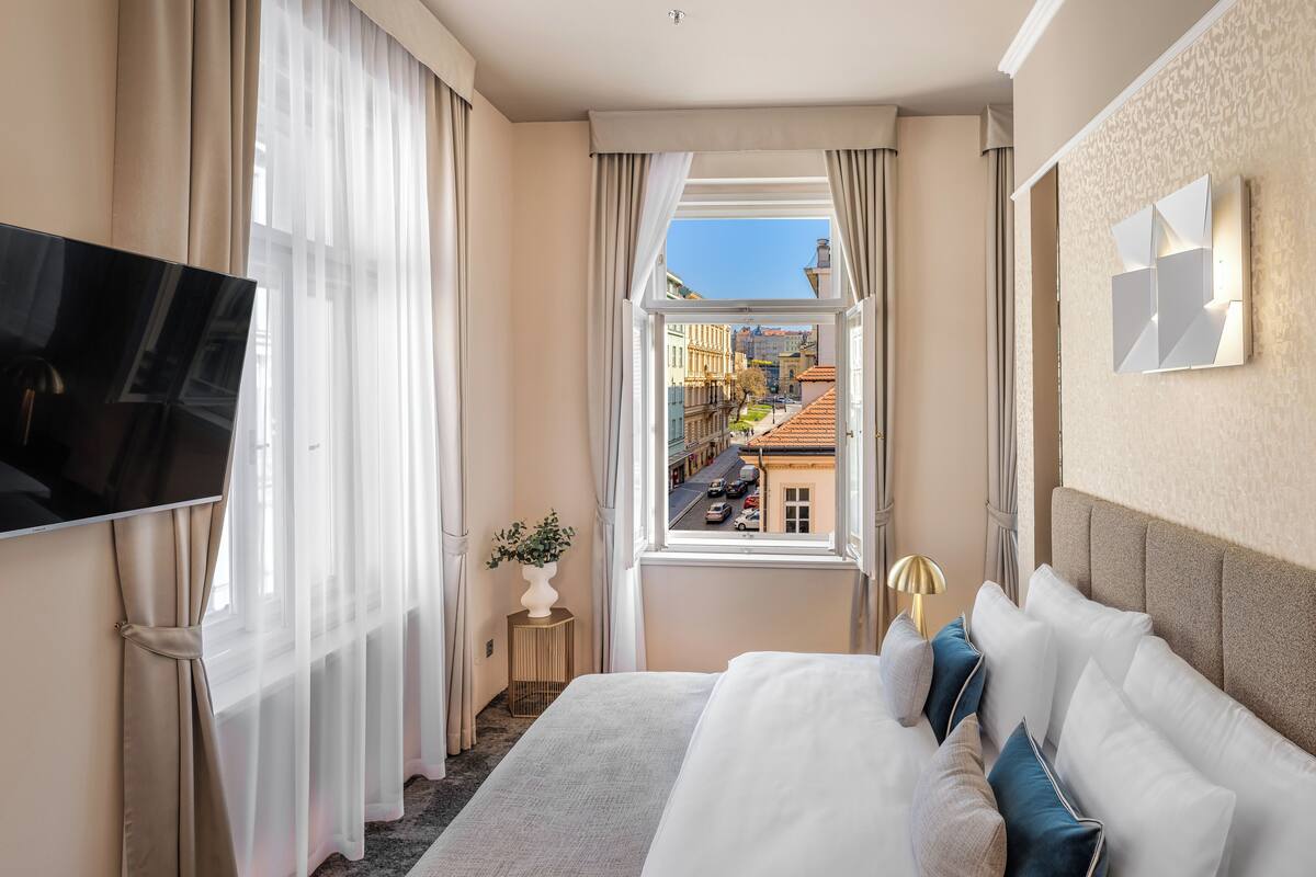Une chambre d’hôtel avec un grand lit, une télévision, une fenêtre donnant sur la ville et une petite table avec une plante.
