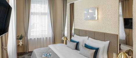 Habitación de hotel con una cama grande, un televisor de pantalla plana, una mesita de noche con lámpara y una ventana con cortinas.
