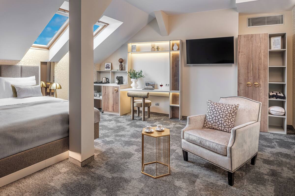 Une chambre d’hôtel moderne dotée d’un grand lit, d’un bureau, d’une chaise, d’une télévision et d’une fenêtre de toit.