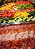 Balcão de charcutaria com diversos tipos de carne e legumes frescos.