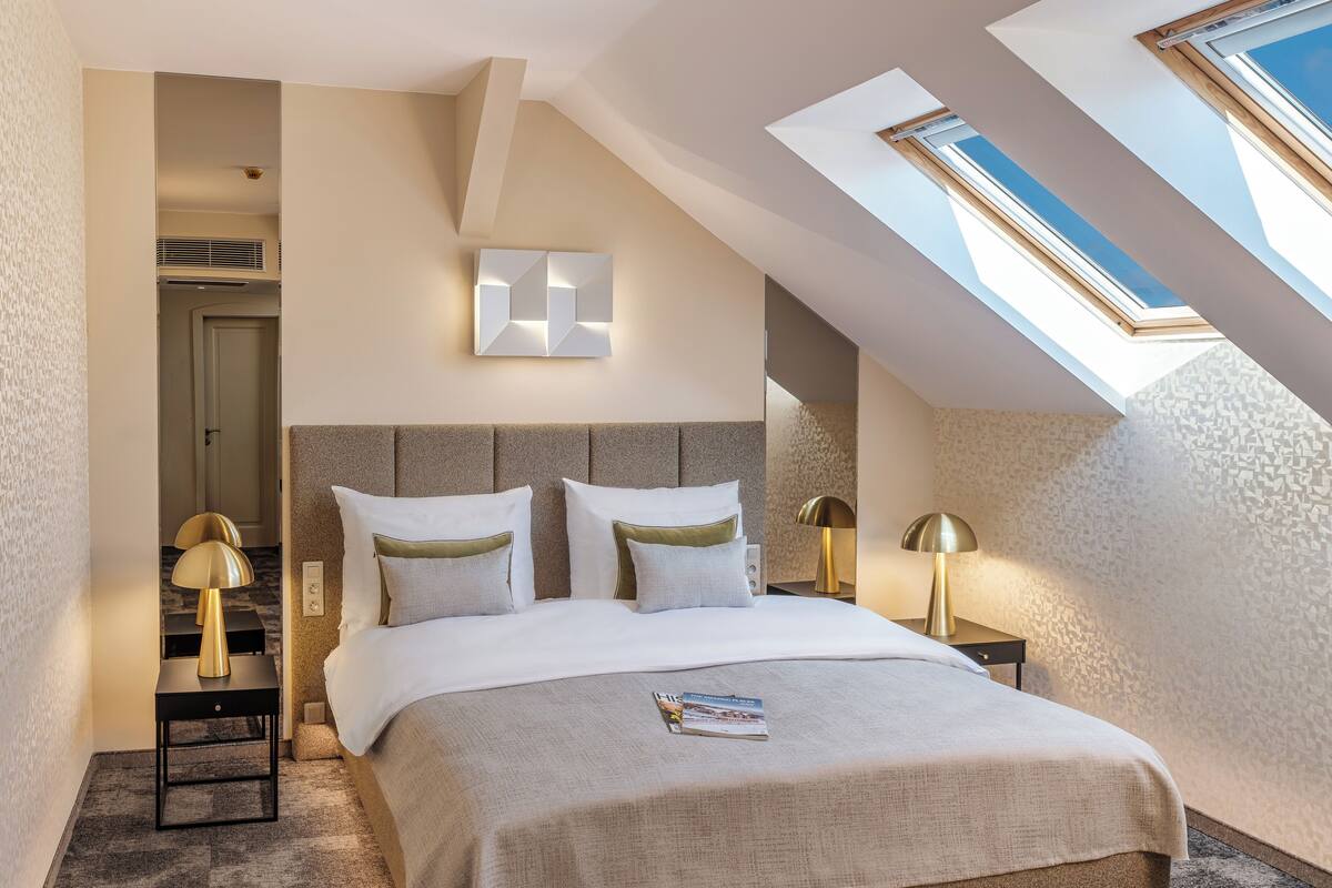 Une chambre d’hôtel moderne avec une lucarne, un grand lit avec une literie blanche et deux tables de chevet avec des lampes.