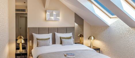 A modern hotel room with a skylight, a large bed with white bedding, and two bedside tables with lamps.