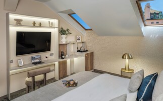 Um quarto moderno com claraboia, uma cama, uma escrivaninha com um laptop, uma televisão e uma máquina de café.