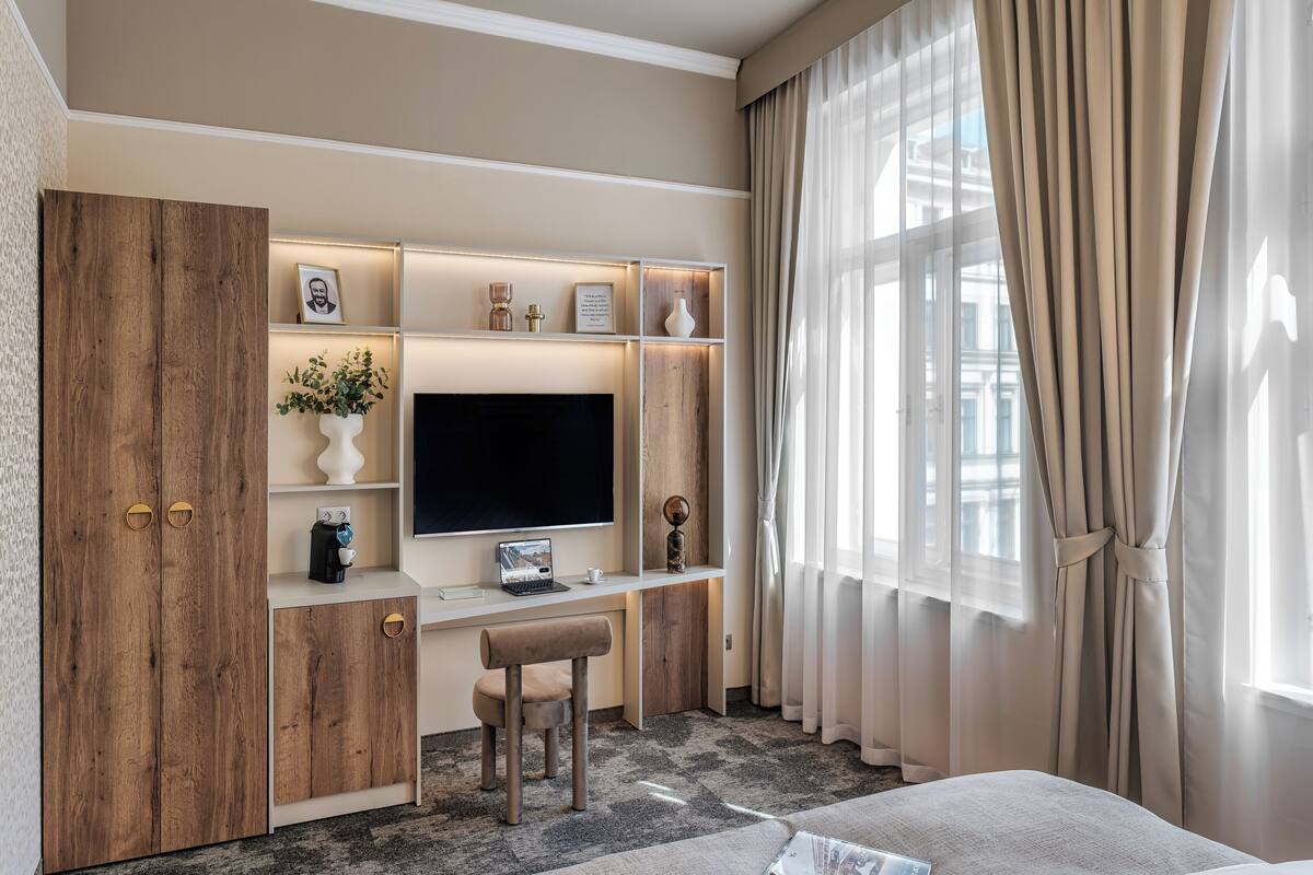 Une chambre d’hôtel moderne dotée d’une grande télévision à écran plat, d’une armoire en bois et d’un bureau avec un ordinateur portable.