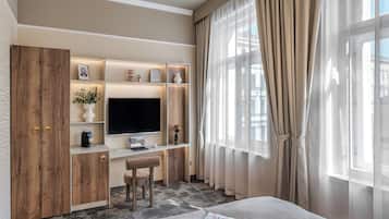 A modern hotel room with a large flat-screen TV, wooden wardrobe, and a desk with a laptop.