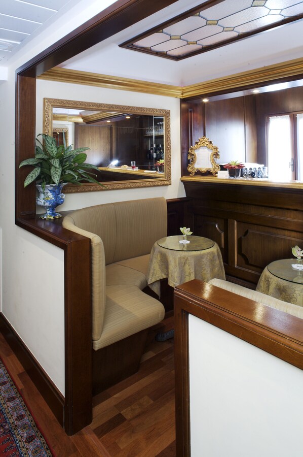 Ein Eckzimmer mit einem beige farbenen Sofa, einem kleinen runden Tisch mit Glasplatte, einem großen Spiegel und einem Holzschrank.
