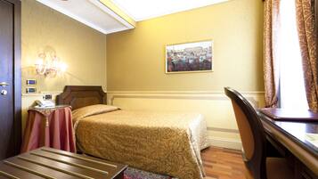 Quarto de hotel com cama, escrivaninha, cadeira, mesa com telefone e quadro na parede.