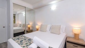 Una cama bien tendida con un edredón estampado, una lámpara de noche y un espejo en la pared.