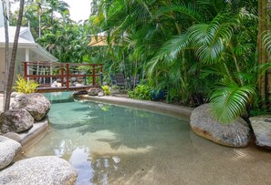 Un área de piscina tranquila con agua cristalina, rodeada de vegetación exuberante y rocas.