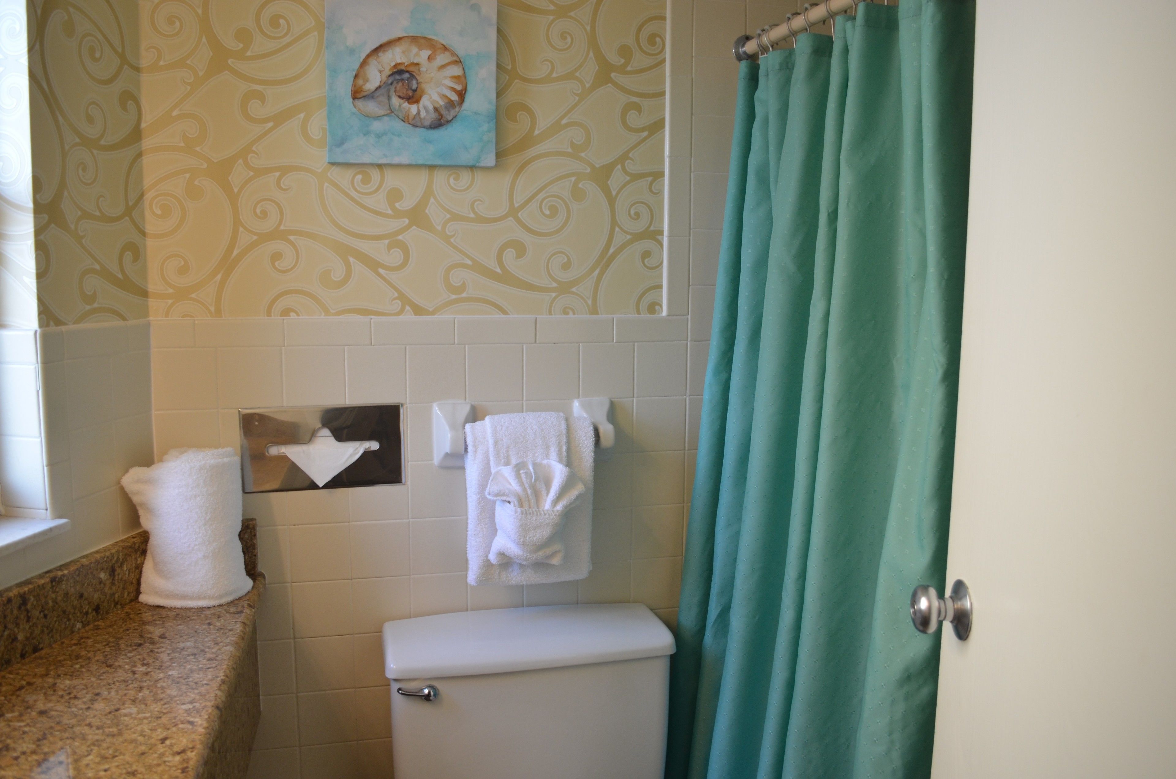 Een badkamer met toilet, een handdoekrek met handdoeken, een decoratieve wand en een blauwgroen douchegordijn.