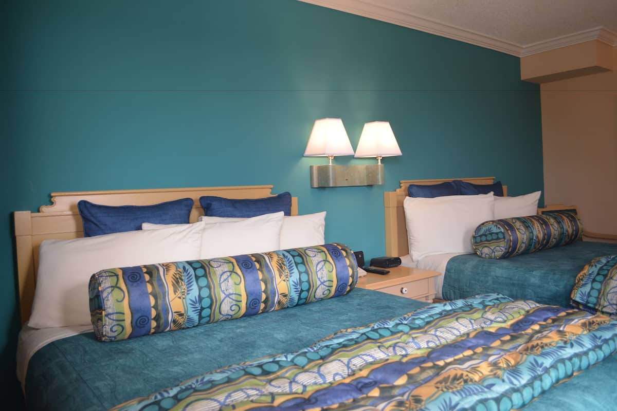 A hotel room with two beds, teal walls, and matching bedding.