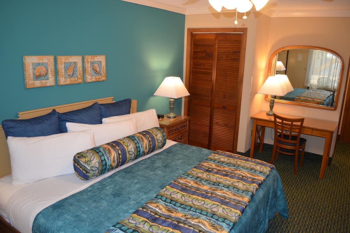A hotel room with a bed, a desk, a chair, a mirror, and a door.