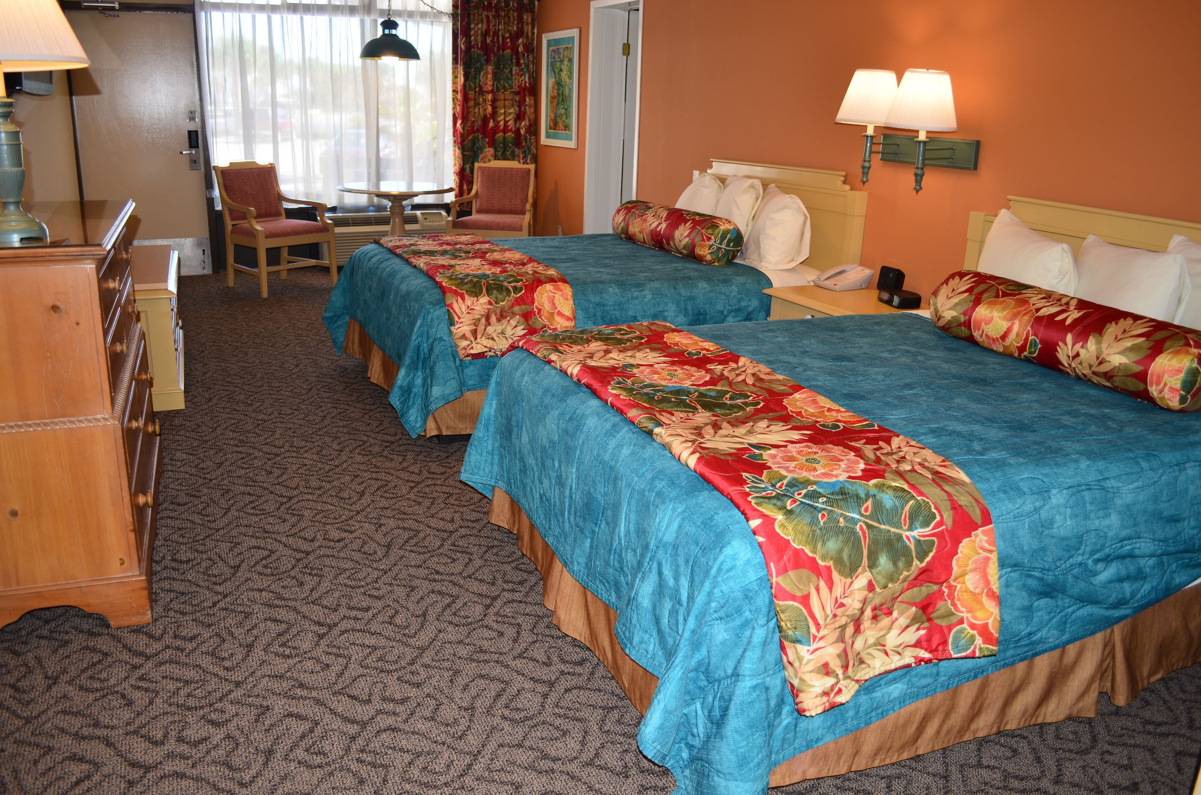A hotel room with two beds, a desk, a chair, and a dresser.