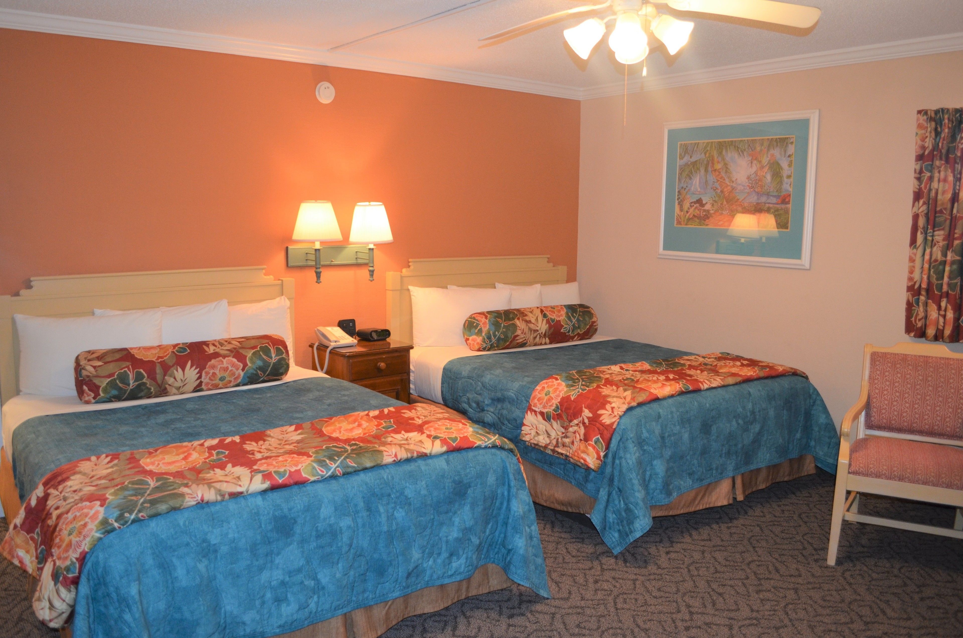A hotel room with two beds, a chair, a nightstand, and a ceiling fan.