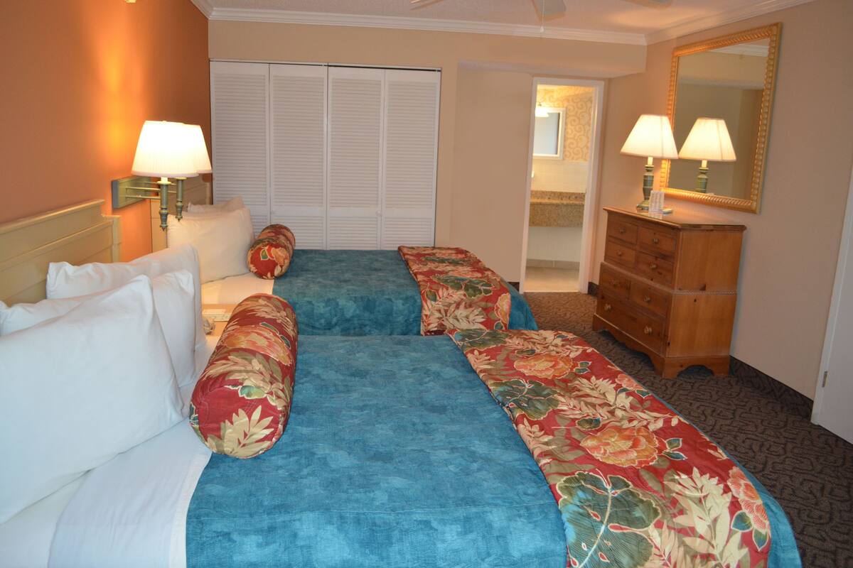 A hotel room with two beds, a dresser, a mirror, and a door leading to a bathroom.