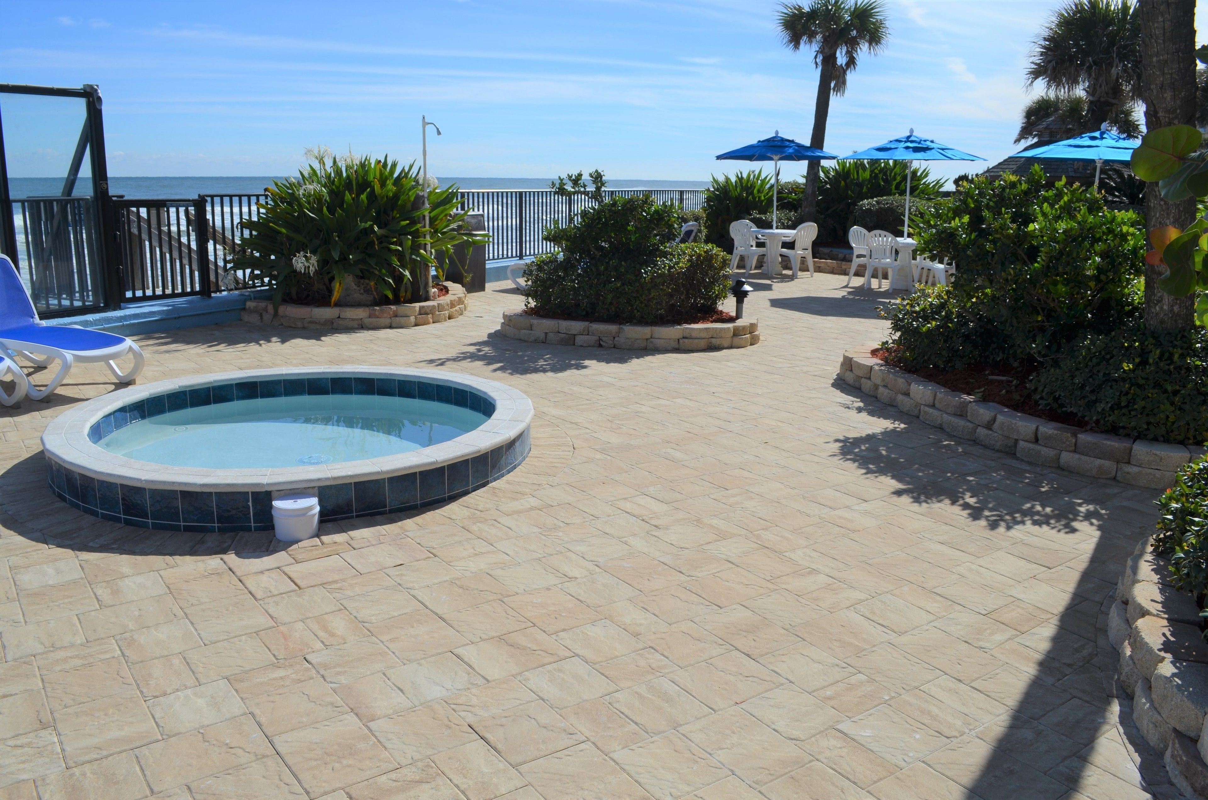 Un área de piscina con jacuzzi, sillones reclinables y sombrillas.