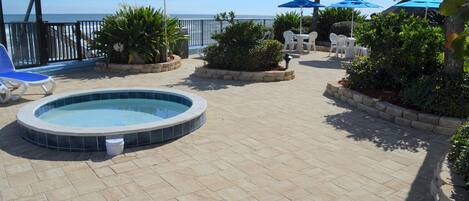 A pool area with a hot tub, lounge chairs, and umbrellas.