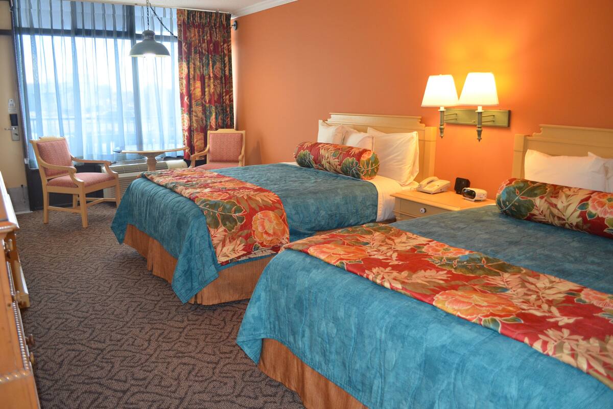 A hotel room with two beds, a desk, a chair, and a telephone.