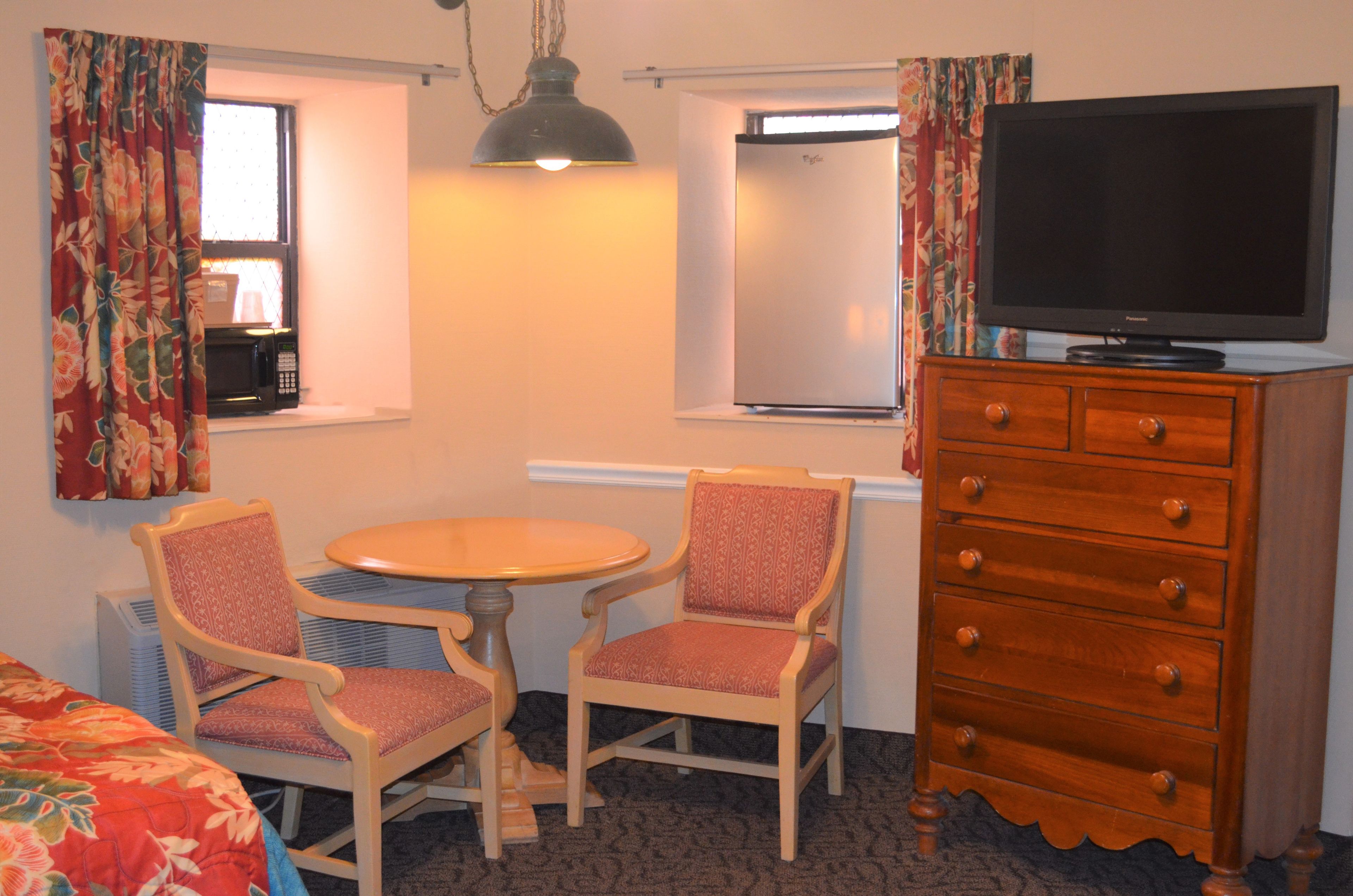A hotel room with a bed, a desk with a chair, a television on a dresser, and a window with curtains.