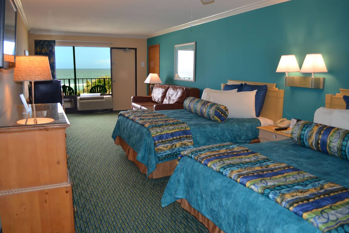 A hotel room with two beds, a desk, a chair, a TV, and a view of the ocean.