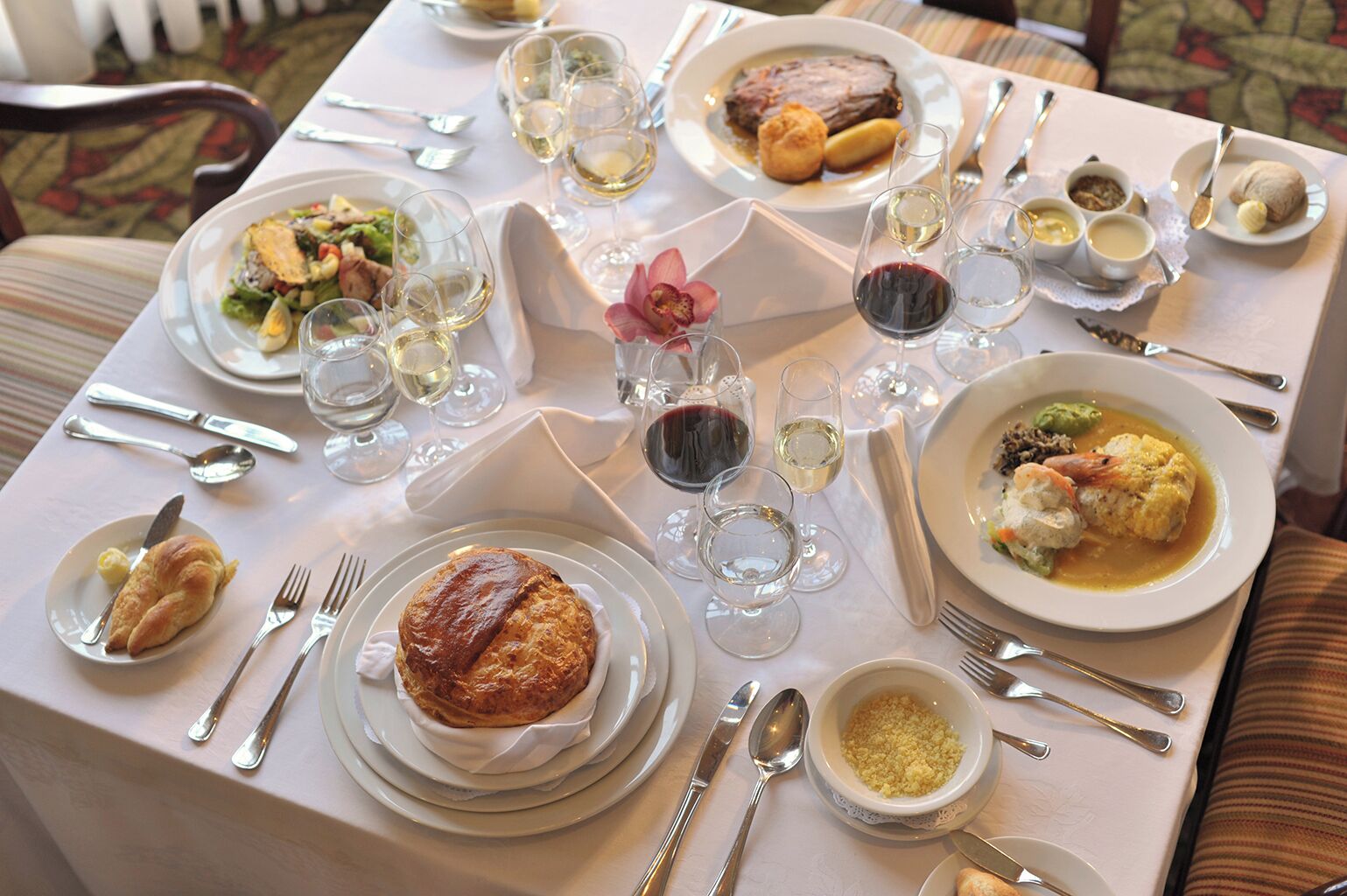 A dining table set with various dishes, glasses of wine, and silverware.