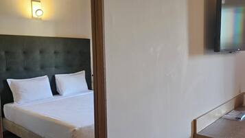 A hotel room with a bed, a television mounted on the wall, and a wooden ceiling.